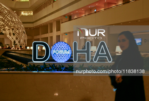 A woman walks past the Doha Forum logo inside the Sheraton Grand Doha Resort & Convention Hotel ahead of the 22nd edition of the Doha Forum...