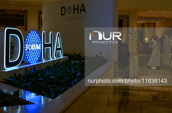 People walk past the Doha Forum logo inside the Sheraton Grand Doha Resort & Convention Hotel ahead of the 22nd edition of the Doha Forum in...