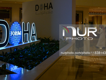 People walk past the Doha Forum logo inside the Sheraton Grand Doha Resort & Convention Hotel ahead of the 22nd edition of the Doha Forum in...