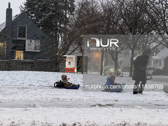 A father pulls his two children on plastic sleds during a snowfall in Toronto, Ontario, Canada, on December 5, 2024. 