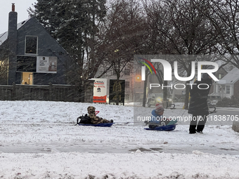 A father pulls his two children on plastic sleds during a snowfall in Toronto, Ontario, Canada, on December 5, 2024. (