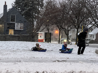 A father pulls his two children on plastic sleds during a snowfall in Toronto, Ontario, Canada, on December 5, 2024. (