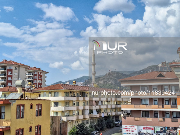 A mosque tower stands between city buildings with mountains in the background in Alanya, Turkey, on November 4, 2024 