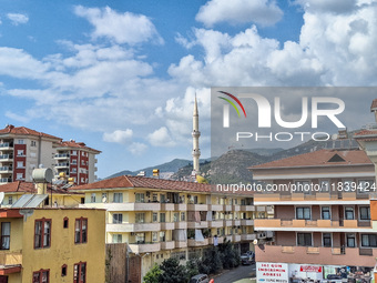 A mosque tower stands between city buildings with mountains in the background in Alanya, Turkey, on November 4, 2024 (