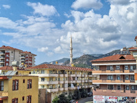 A mosque tower stands between city buildings with mountains in the background in Alanya, Turkey, on November 4, 2024 (