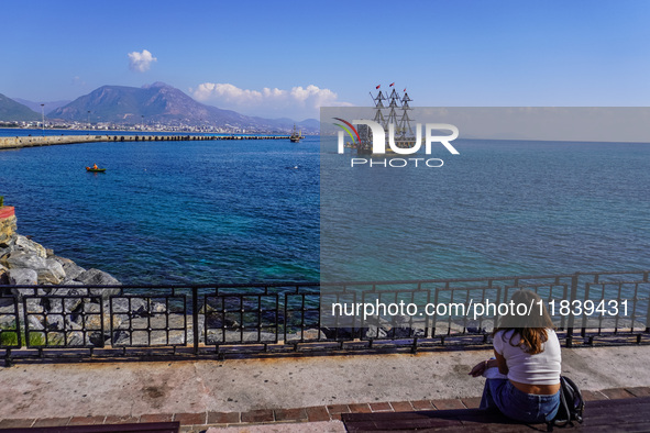 A young woman sits on a bench and looks at a tourist boat sailing in the Mediterranean Sea in Alanya, Turkey, on November 5, 2024. 