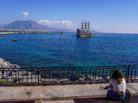 A young woman sits on a bench and looks at a tourist boat sailing in the Mediterranean Sea in Alanya, Turkey, on November 5, 2024. (