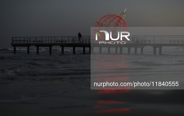 People walk on a pier in front of a giant illuminated Christmas ball in Larnaca. Cyprus, Friday, December 6, 2024 