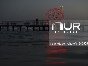 People walk on a pier in front of a giant illuminated Christmas ball in Larnaca. Cyprus, Friday, December 6, 2024 (