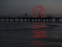 People walk on a pier in front of a giant illuminated Christmas ball in Larnaca. Cyprus, Friday, December 6, 2024 (