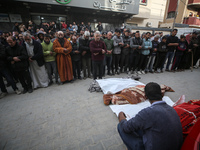 Palestinians pray by the bodies of relatives killed in Israeli strikes during a funeral at the al-Awda Hospital at the Nuseirat refugee Camp...