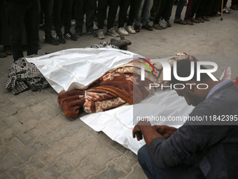 Palestinians pray by the bodies of relatives killed in Israeli strikes during a funeral at the al-Awda Hospital at the Nuseirat refugee Camp...