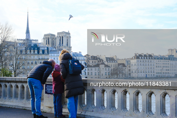 A family observes Notre-Dame Cathedral from a bridge on Ile Saint-Louis. 