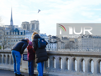 A family observes Notre-Dame Cathedral from a bridge on Ile Saint-Louis. (