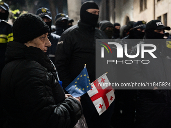 An anti-government protester carries EU and Georgian flags while facing the police during a rally for the tenth consecutive day of mass demo...