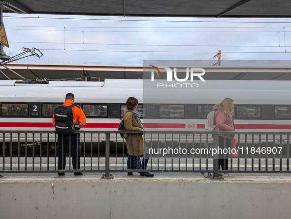 Three travelers stand on a platform at Munich Pasing Station in Bavaria, Germany, on November 15, 2024, looking towards an ICE train situate...