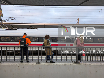 Three travelers stand on a platform at Munich Pasing Station in Bavaria, Germany, on November 15, 2024, looking towards an ICE train situate...