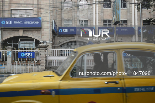 A yellow taxi passes next to an SBI bank branch in Kolkata, India, on December 8, 2024. 