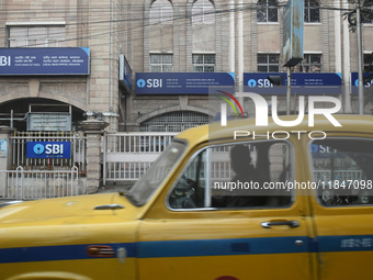 A yellow taxi passes next to an SBI bank branch in Kolkata, India, on December 8, 2024. (