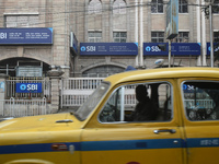 A yellow taxi passes next to an SBI bank branch in Kolkata, India, on December 8, 2024. (