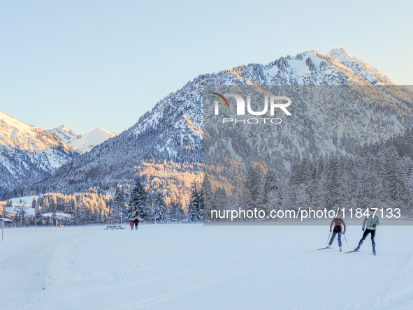 In Oberstdorf, Bavaria, Germany, on January 20, 2024, skiers glide across a flat, snow-covered trail surrounded by alpine scenery. The snow-...