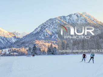 In Oberstdorf, Bavaria, Germany, on January 20, 2024, skiers glide across a flat, snow-covered trail surrounded by alpine scenery. The snow-...