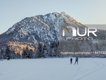 In Oberstdorf, Bavaria, Germany, on January 20, 2024, skiers glide across a flat, snow-covered trail surrounded by alpine scenery. The snow-...