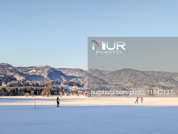 In Oberstdorf, Bavaria, Germany, on January 20, 2024, skiers glide across a flat, snow-covered trail surrounded by alpine scenery. The snow-...