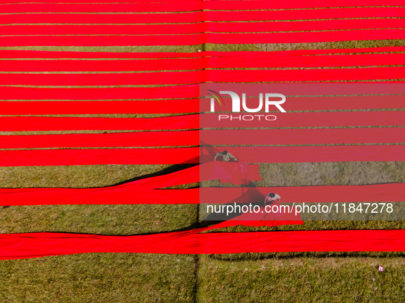 An aerial view shows people working in a field, stretching red cloth in Narsingdi, Dhaka, Bangladesh, on December 8, 2024. This fabric is co...