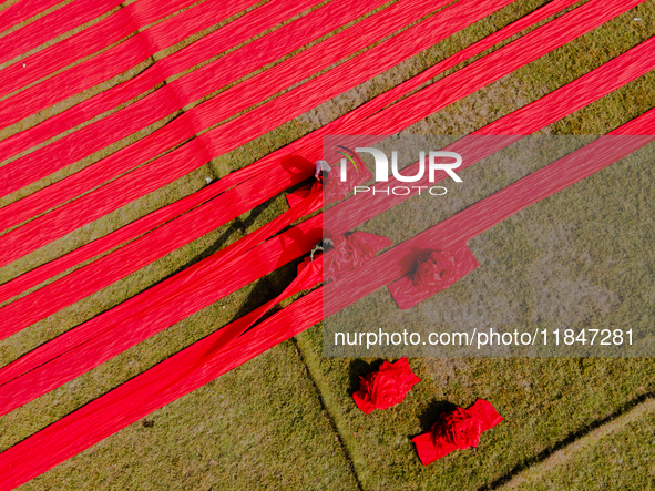 An aerial view shows people working in a field, stretching red cloth in Narsingdi, Dhaka, Bangladesh, on December 8, 2024. This fabric is co...