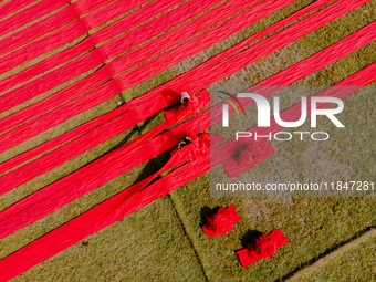 An aerial view shows people working in a field, stretching red cloth in Narsingdi, Dhaka, Bangladesh, on December 8, 2024. This fabric is co...