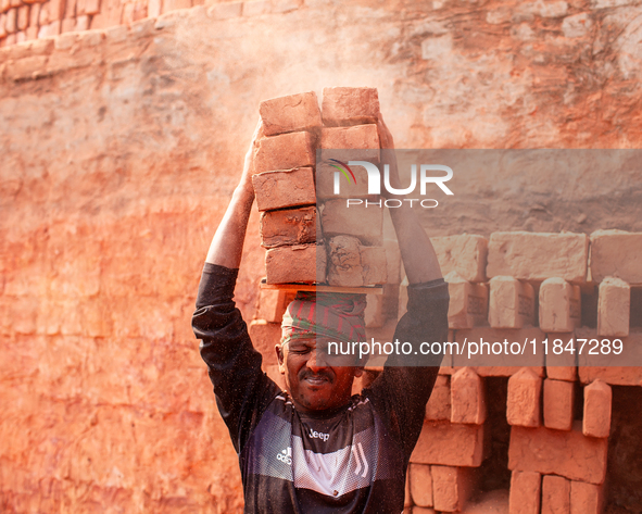 In Narsingdi, Dhaka, Bangladesh, on December 8, 2024, laborers carry piles of bricks weighing more than 15 kg on their heads in a brick kiln...