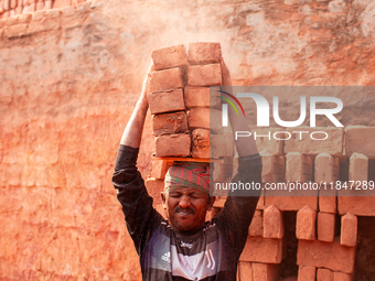 In Narsingdi, Dhaka, Bangladesh, on December 8, 2024, laborers carry piles of bricks weighing more than 15 kg on their heads in a brick kiln...