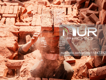 In Narsingdi, Dhaka, Bangladesh, on December 8, 2024, laborers carry piles of bricks weighing more than 15 kg on their heads in a brick kiln...