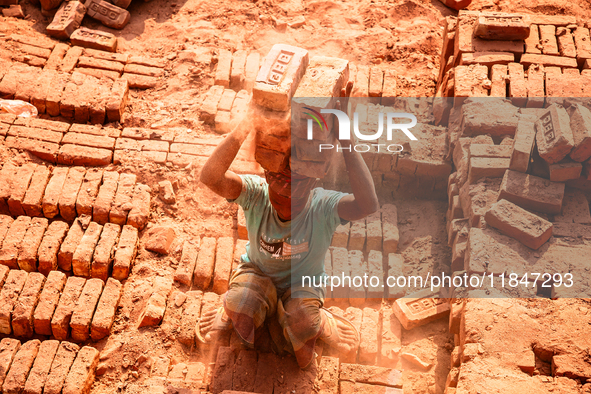 In Narsingdi, Dhaka, Bangladesh, on December 8, 2024, laborers carry piles of bricks weighing more than 15 kg on their heads in a brick kiln...