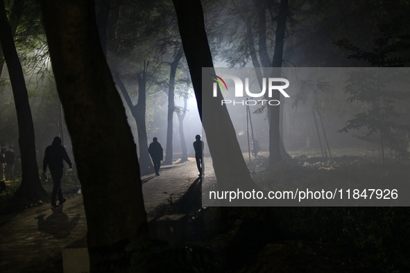 People walk through a park covered in light fog as winter begins in Dhaka, Bangladesh, on December 8, 2024. 