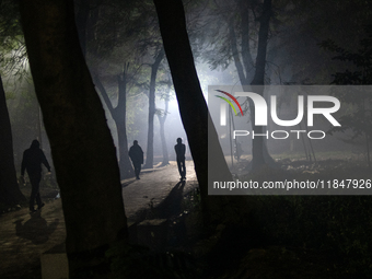 People walk through a park covered in light fog as winter begins in Dhaka, Bangladesh, on December 8, 2024. (