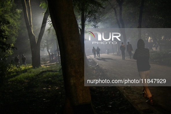 People walk through a park covered in light fog as winter begins in Dhaka, Bangladesh, on December 8, 2024. 