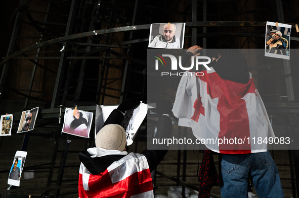 An anti-government protester fixes a placard on a partially installed artificial Christmas tree among pictures of individuals reportedly bea...