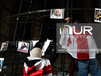 An anti-government protester fixes a placard on a partially installed artificial Christmas tree among pictures of individuals reportedly bea...