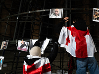 An anti-government protester fixes a placard on a partially installed artificial Christmas tree among pictures of individuals reportedly bea...