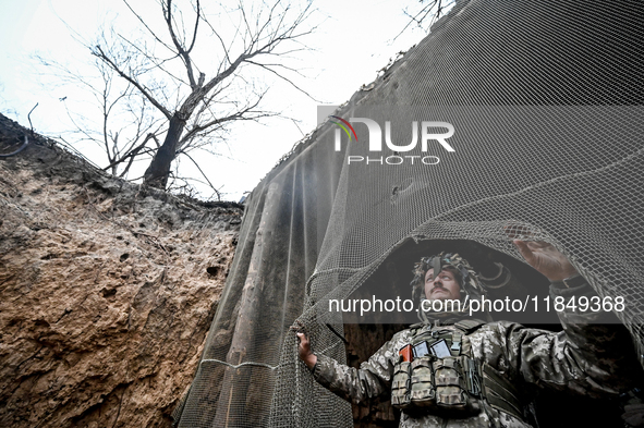 An artilleryman of Ukraine's 118th Separate Mechanized Brigade stands by a net that masks the space where a self-propelled howitzer is kept...