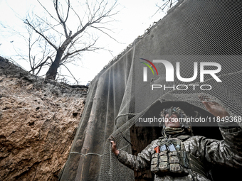 An artilleryman of Ukraine's 118th Separate Mechanized Brigade stands by a net that masks the space where a self-propelled howitzer is kept...