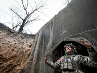 An artilleryman of Ukraine's 118th Separate Mechanized Brigade stands by a net that masks the space where a self-propelled howitzer is kept...