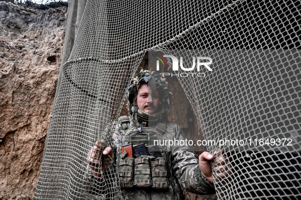 An artilleryman of Ukraine's 118th Separate Mechanized Brigade stands by a net that masks the space where a self-propelled howitzer is kept...