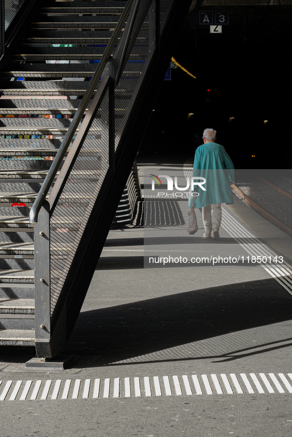 A senior citizen in a turquoise coat walks along a train platform under the shadow of a staircase in Zurich, Switzerland, on March 29, 2024....