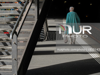 A senior citizen in a turquoise coat walks along a train platform under the shadow of a staircase in Zurich, Switzerland, on March 29, 2024....