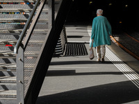 A senior citizen in a turquoise coat walks along a train platform under the shadow of a staircase in Zurich, Switzerland, on March 29, 2024....