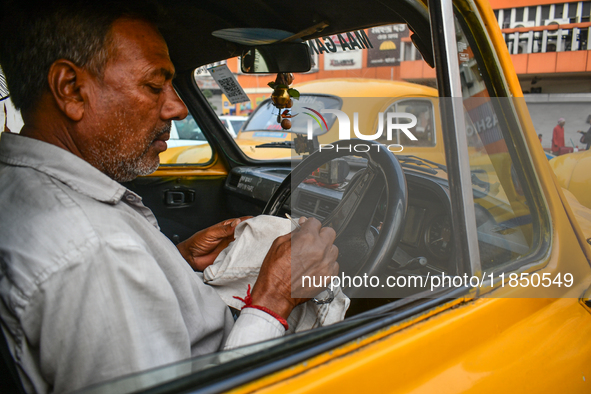 A taxi driver sits inside his yellow taxi, waiting for customers near Sealdah railway station in Kolkata, India. 