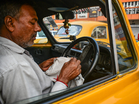 A taxi driver sits inside his yellow taxi, waiting for customers near Sealdah railway station in Kolkata, India. (